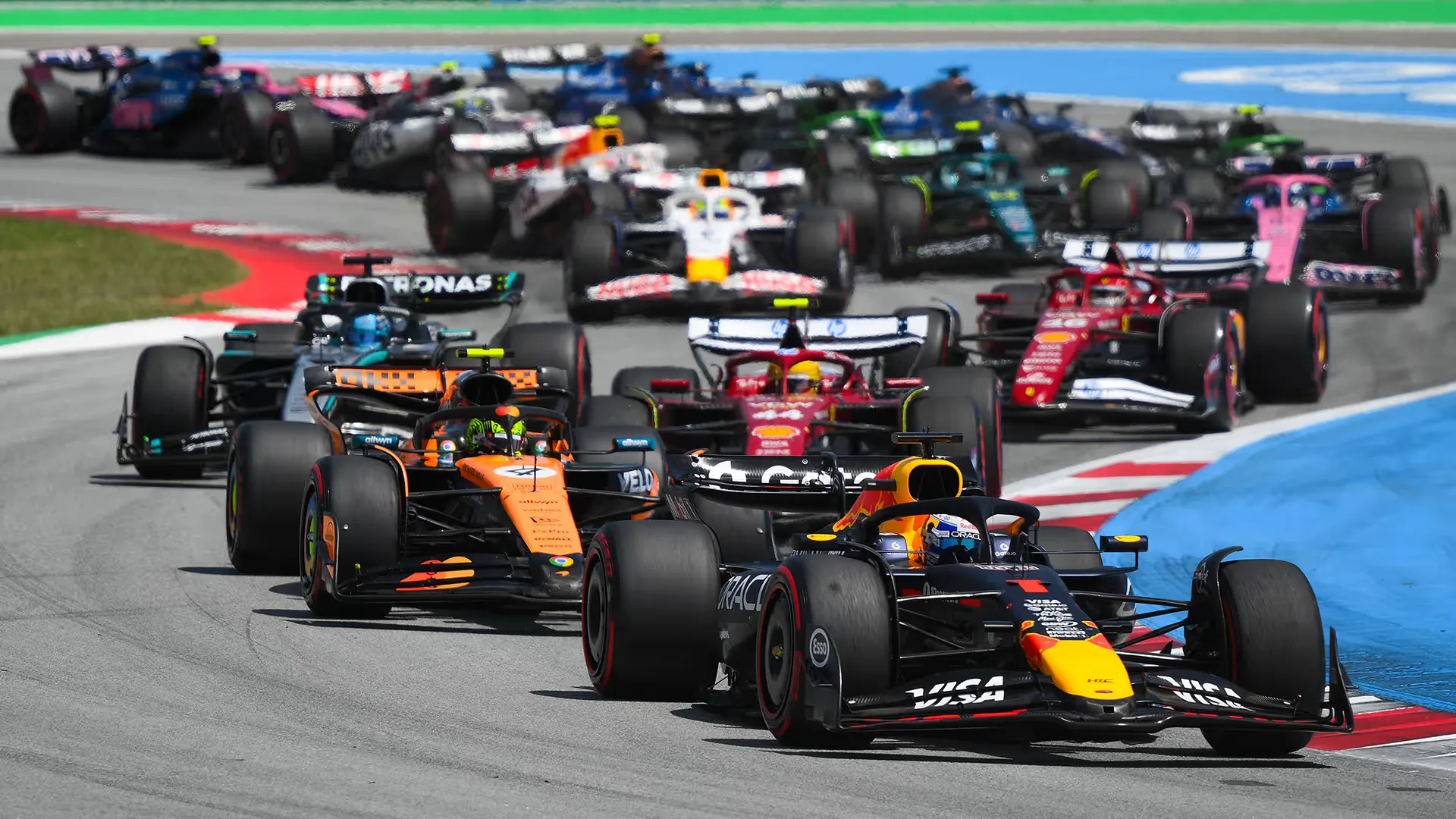 a pack of formula 1 cars funnels into a first corner, a red bull ahead of two mclarens and a ferrari