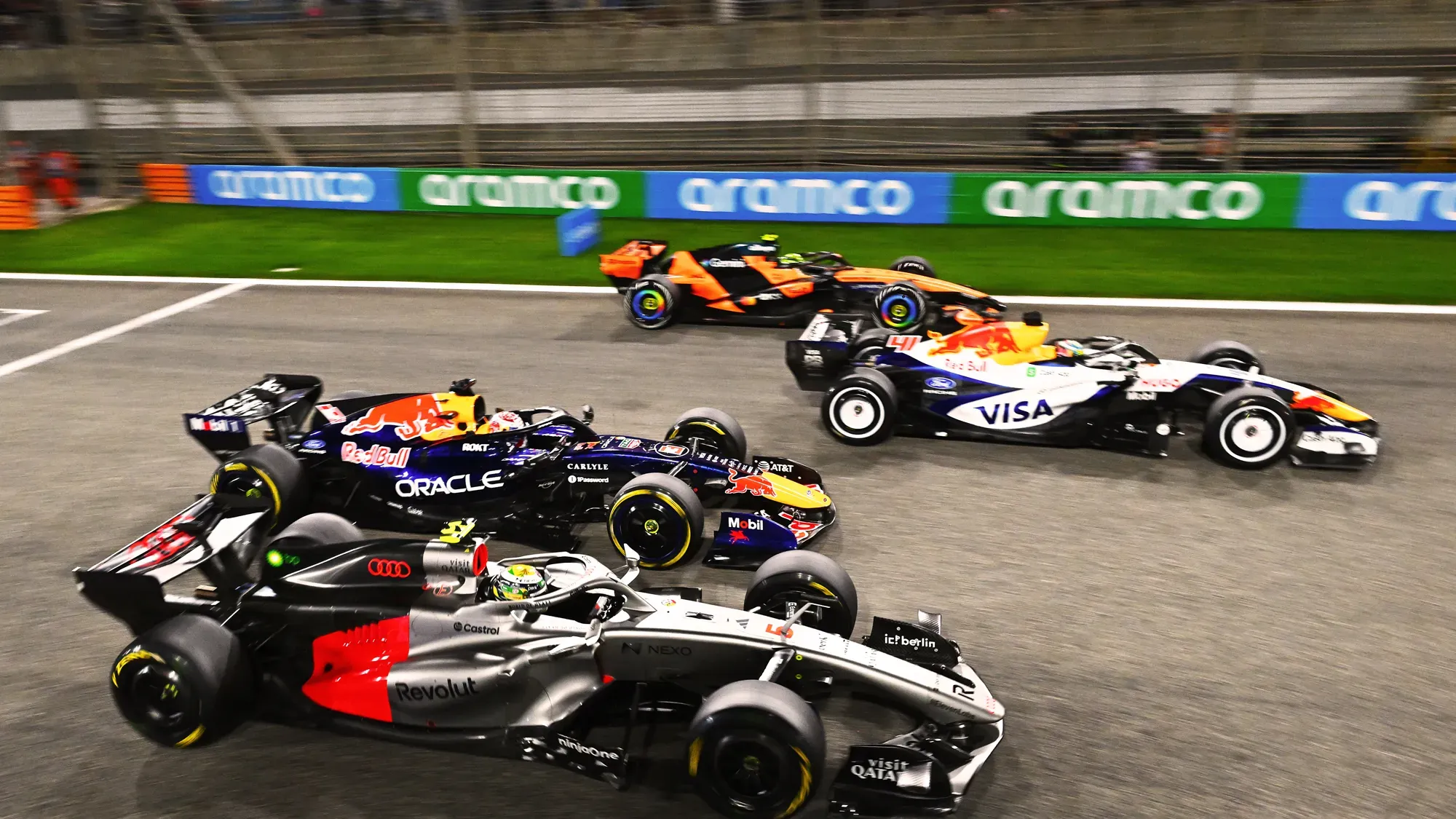 four cars squeeze through a corner side by side under floodlights